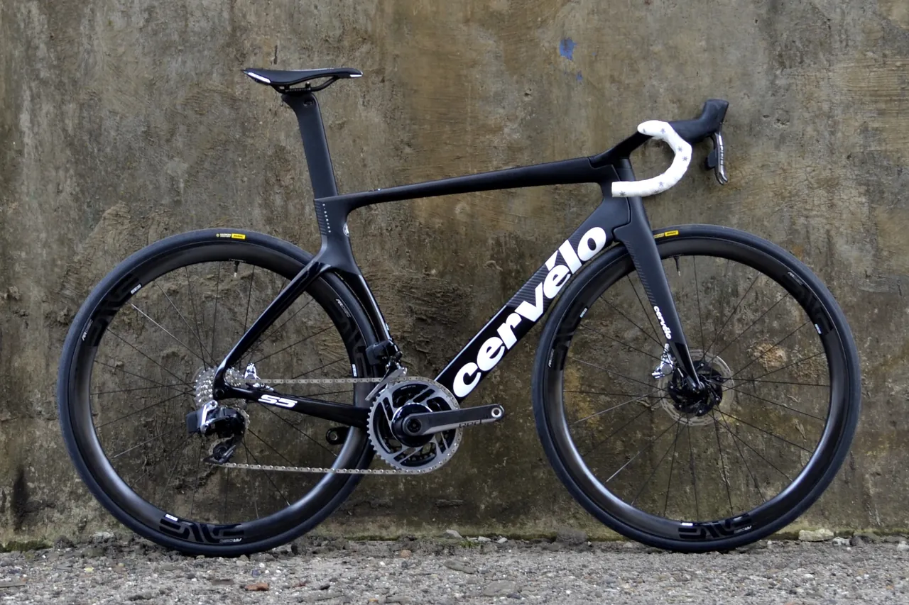 Black Cervélo S5 aero road bike with deep carbon wheels and disc brakes, leaning against a concrete wall
