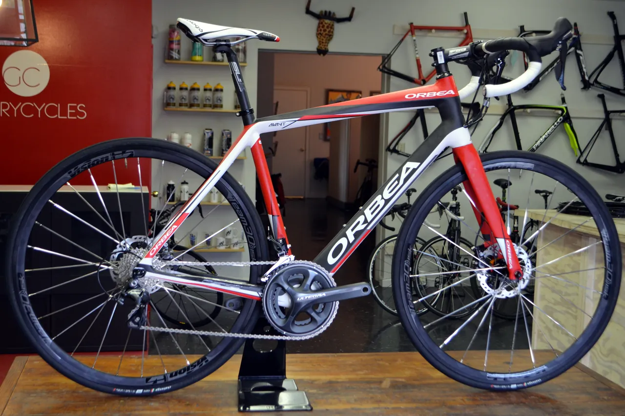 Red, white and black Orbea Avant road bike with disc brakes on a stand inside a bicycle shop