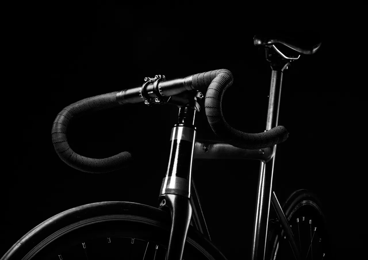 Black-and-white close-up of a road bike frame and drop handlebars against a black background