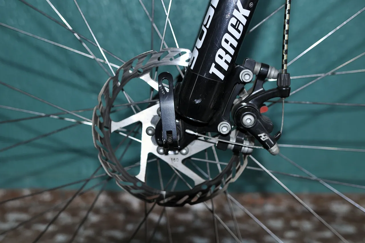Mechanical disc brake caliper on a black front fork, gripping the disc brake rotor
