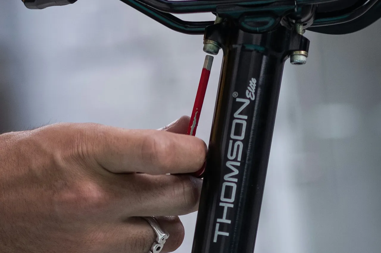 Black seatpost with its saddle clamp being adjusted with a hex key