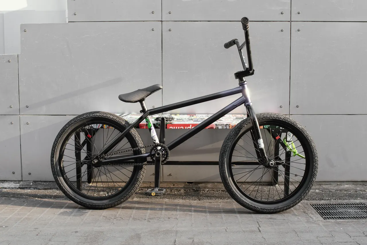 Black BMX bike with high-rise handlebars and 20-inch tyres parked against a grey panelled wall