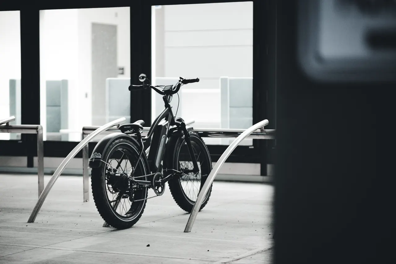 Black electric bike with wide tyres and a frame-mounted battery parked at a bike rack