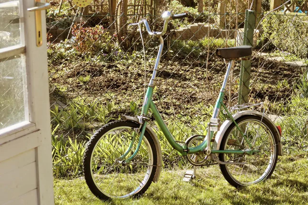 Green folding bike with small wheels and a hinged frame parked in a garden