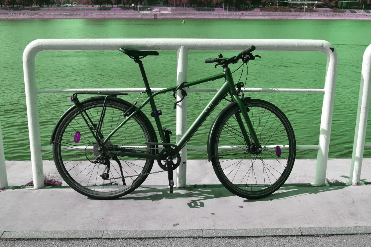 Dark green hybrid bike with flat handlebars and a rear rack parked by a white railing beside a river