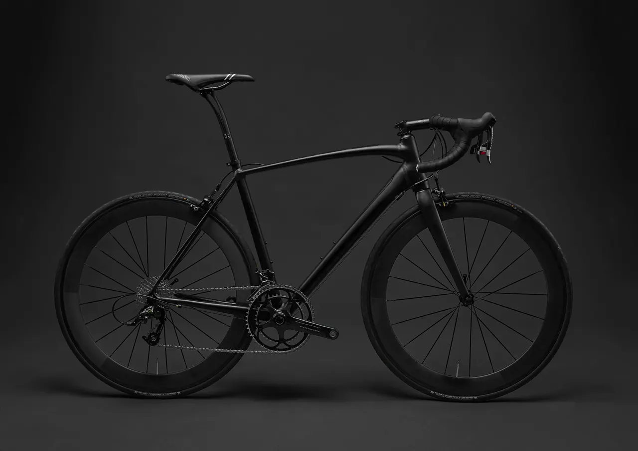 Black road bike with drop handlebars and deep-section wheels on a dark studio background