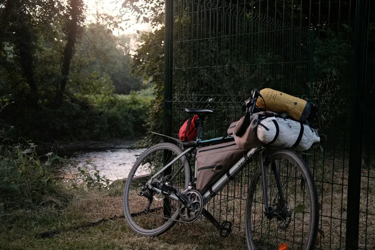 Loaded touring bike with frame, saddle and handlebar bags leaning on a fence by a river